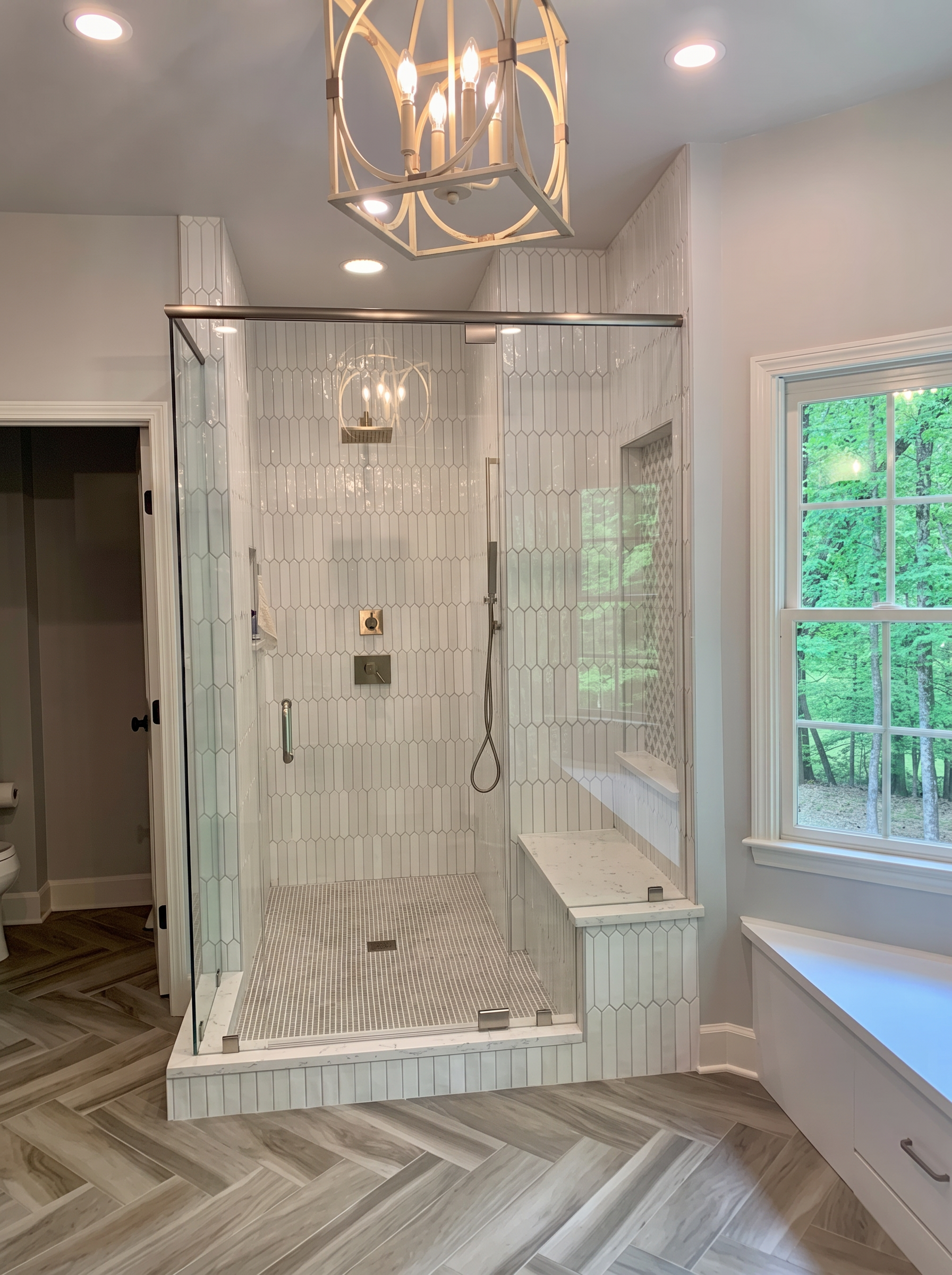 Glass shower with picket tile, built-in bench, and herringbone floor
